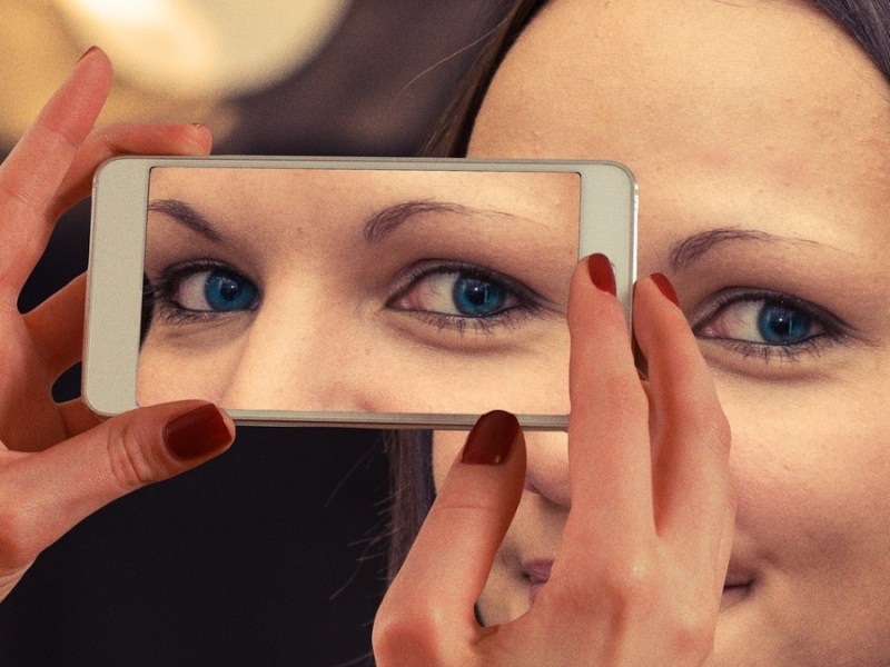 Eine optische Täuschung von einer Frau, die sich ihr Smartphone wie eine Maske vor das Gesicht hält.