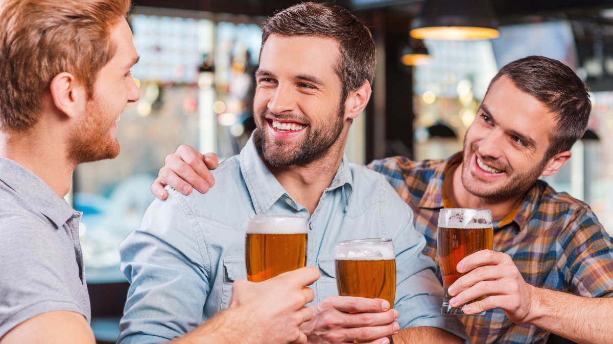 Drei Freunde in einer Kneipe prosten sich mit einem Glas Bier zu.