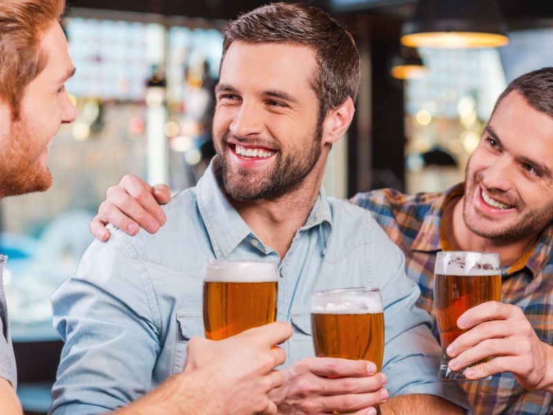 Drei Freunde in einer Kneipe prosten sich mit einem Glas Bier zu.