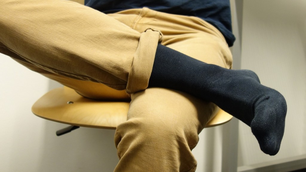 Ein Mann mit beiger Hose sitzt mit überschlagenen Beinen auf einem Stuhl und man sieht seine Socken.