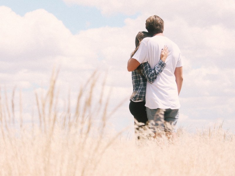 Ein Paar steht Arm in Arm in einem Kornfeld vor einem blauen Himmel.