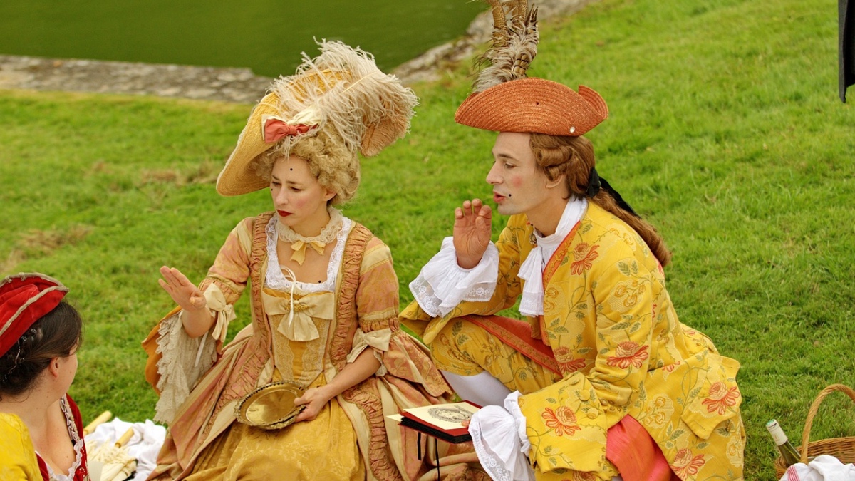Ein Paar in barocker Kleidung bei einem Picknick auf einer Wiese.