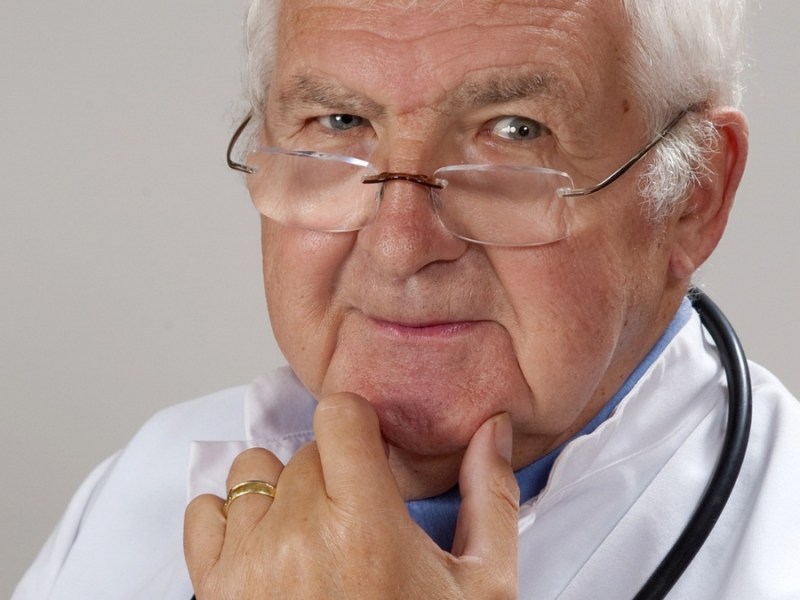 Ein Bild von einem älteren Arzt mit Brille und Stethoskop.