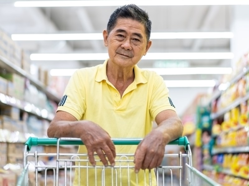 Älterer Mann schiebt Einkaufswagen in Supermarkt.