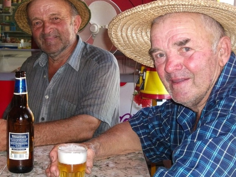Zwei Männer mit Strohhut trinken Bier in einer Kneipe.