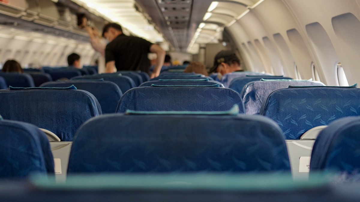 Eine Flugzeugkabine vom Sitz aus fotografiert. Einige Passagiere stehen von ihren Sitzen auf und holen ihr Gepäck aus der Gepäckablage des Flugzeugs.