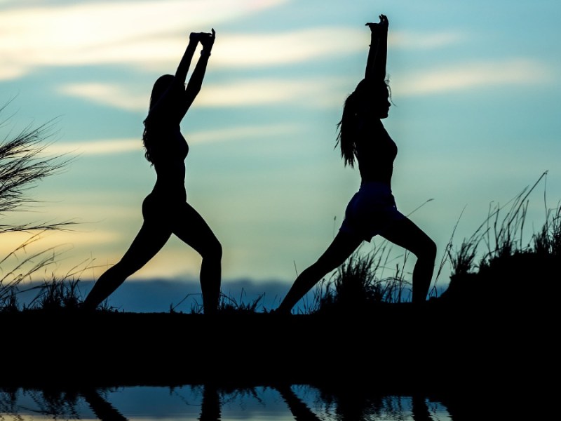 Die Silhouetten zweier Frauen, die in der Abenddämmerung Yoga machen.