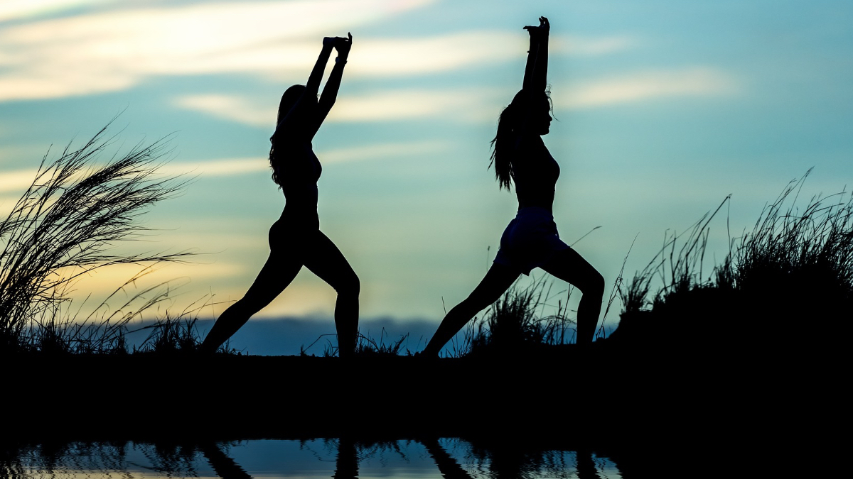 Die Silhouetten zweier Frauen, die in der Abenddämmerung Yoga machen.