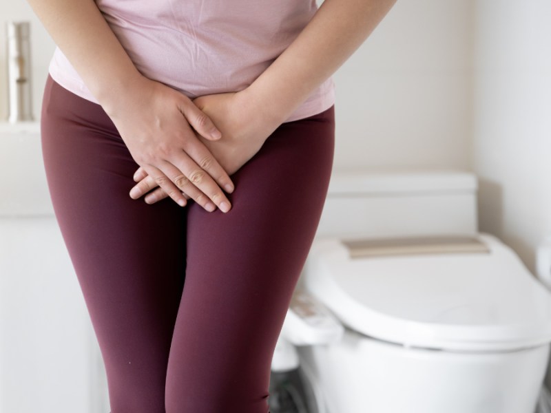 Eine Frau halt sich auf einer Toilette die Hand vor den Bauch.