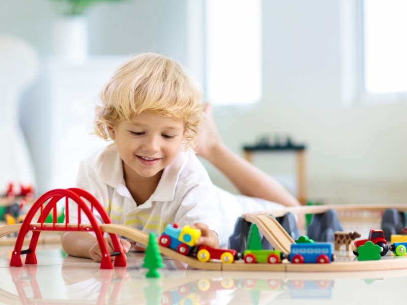 Ein kleiner blonder Junge spielt mit einer Modelleisenbahn aus Holz.