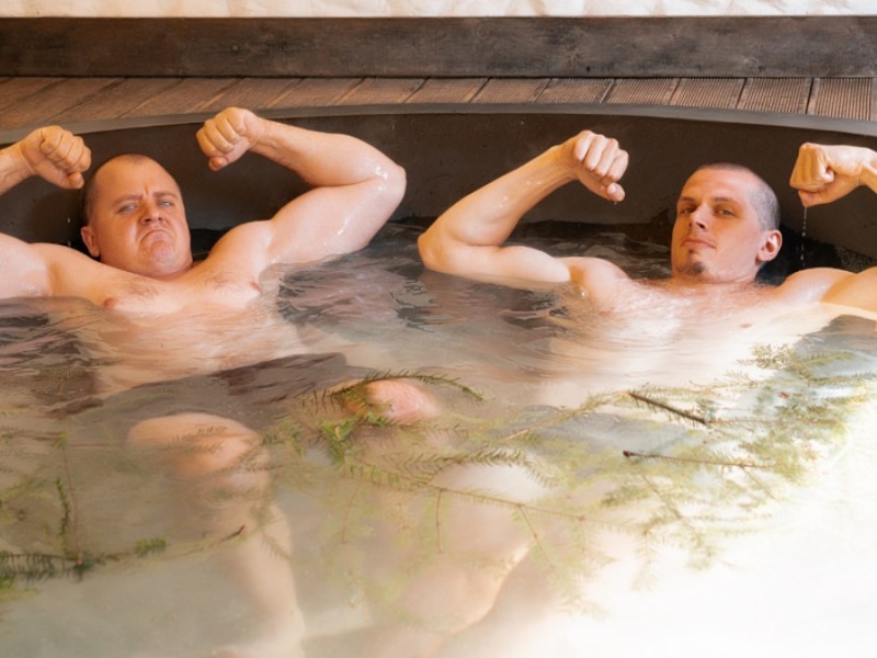 Zwei Männer liegen in einem Whirlpool und spannen ihren Bizeps an.
