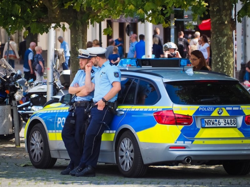 Zwei Polizisten lehnen sich an einem Polizeiwagen an.