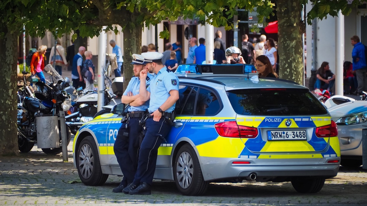 Zwei Polizisten lehnen sich an einem Polizeiwagen an.