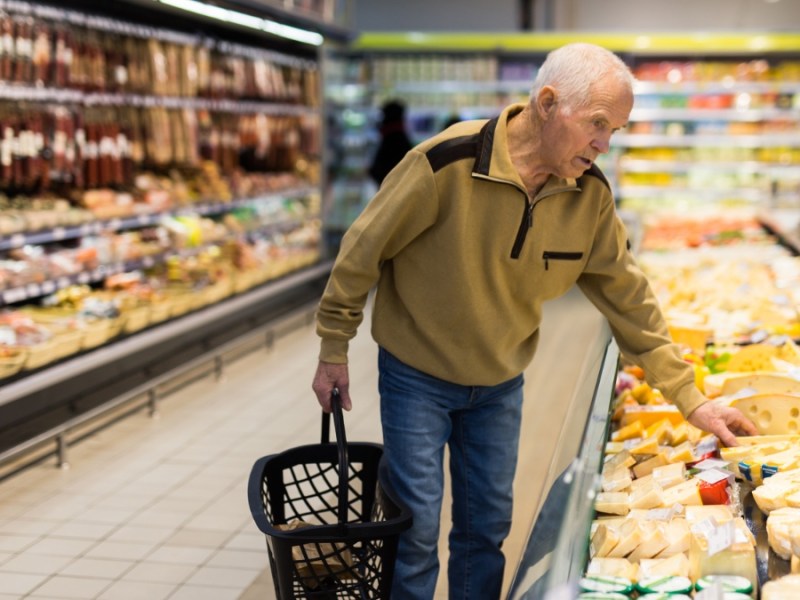 Ein alter Mann kauft Käse in einem Supermarkt ein.