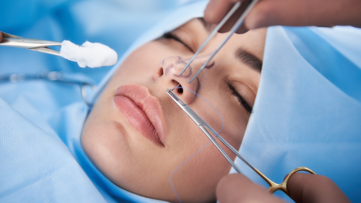 Nahaufnahme einer Frau mit schönen Lippen im Operationssaal. Arzt in Handschuhen hält medizinisches Instrument während einer Nasenkorrektur.