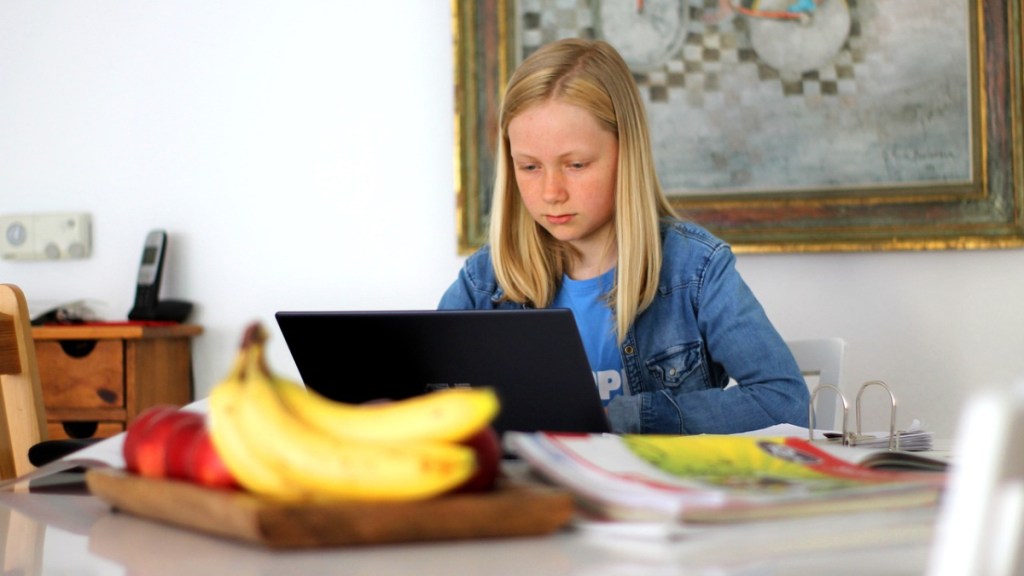 Ein kleines Mädchen sitzt vor einem Laptop und macht seine Hausaufgaben.