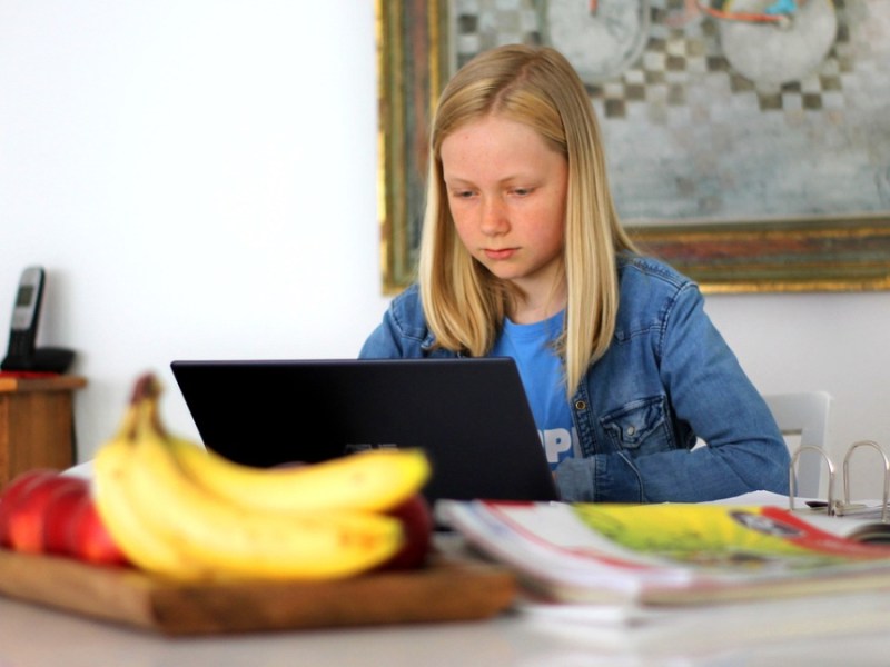 Ein kleines Mädchen sitzt vor einem Laptop und macht seine Hausaufgaben.