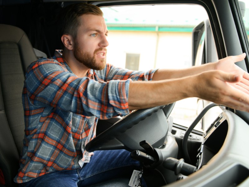 Ein wütender Lkw-Fahrer ruft und gestikuliert hinterm Steuer seines Lastwagens.