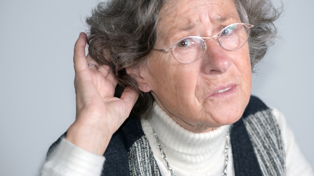 Ein Bild einer schwerhörigen Rentnerin, die sich eine Hand ans rechte Ohr hält.