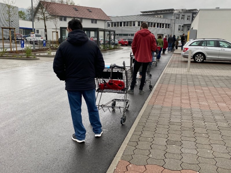Eine Schlange von Menschen mit Einkaufswangen vor einem Supermarkt.
