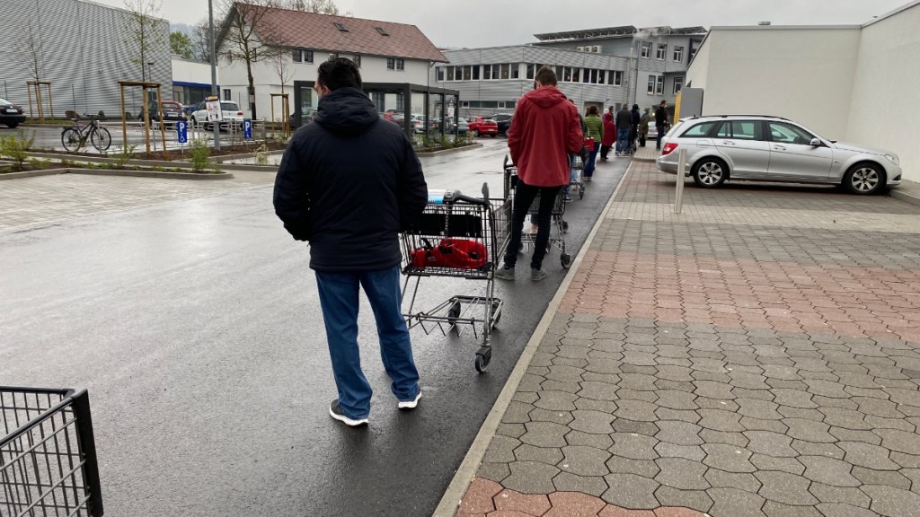 Eine Schlange von Menschen mit Einkaufswangen vor einem Supermarkt.