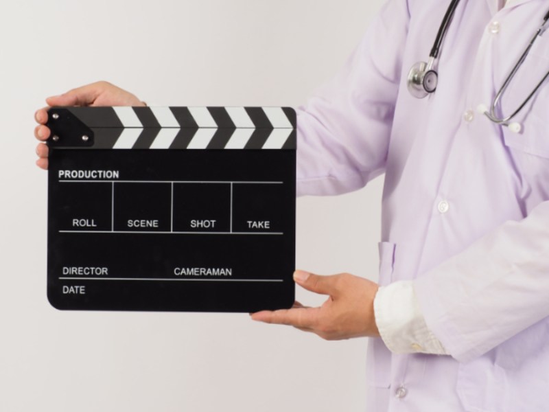 Ein Arzt hält eine Filmklappe in den Händen.