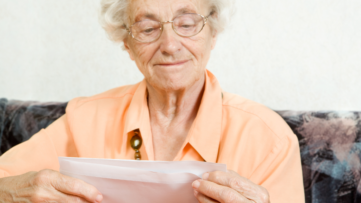 Eine Seniorin öffnet freudig einen Briefumschlag.