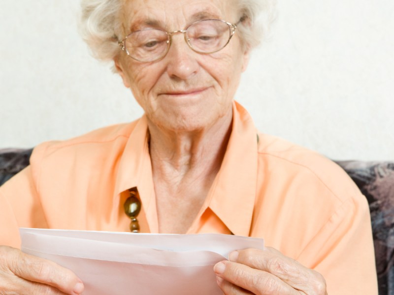 Eine Seniorin öffnet freudig einen Briefumschlag.