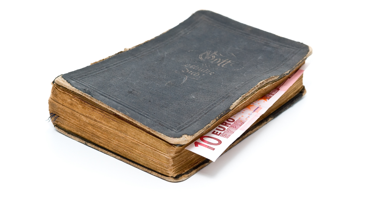 Ein Bild von einer alten Bibel mit einem Zehn-Euro-Schein als Lesezeichen.
