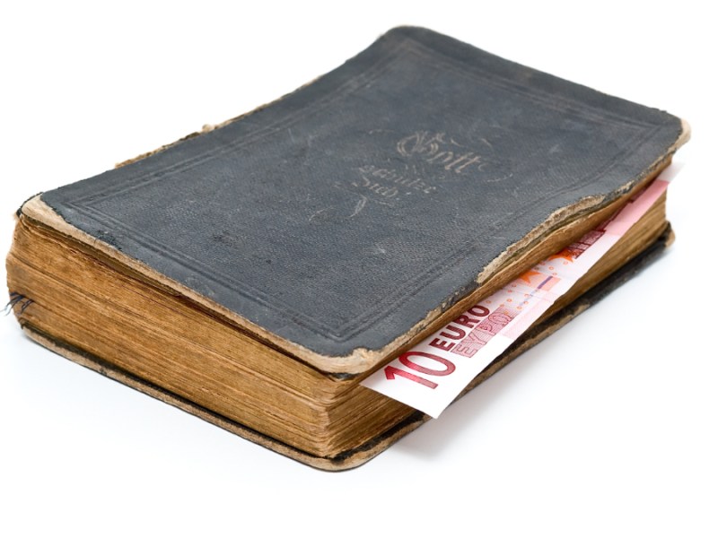 Ein Bild von einer alten Bibel mit einem Zehn-Euro-Schein als Lesezeichen.