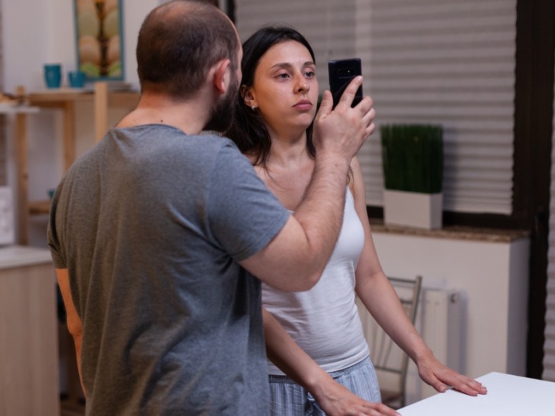 Ein Mann zeigt einer Frau sein Smartphone, auf den ein Nachweis zu sehen ist, dass sie ihn betrog.