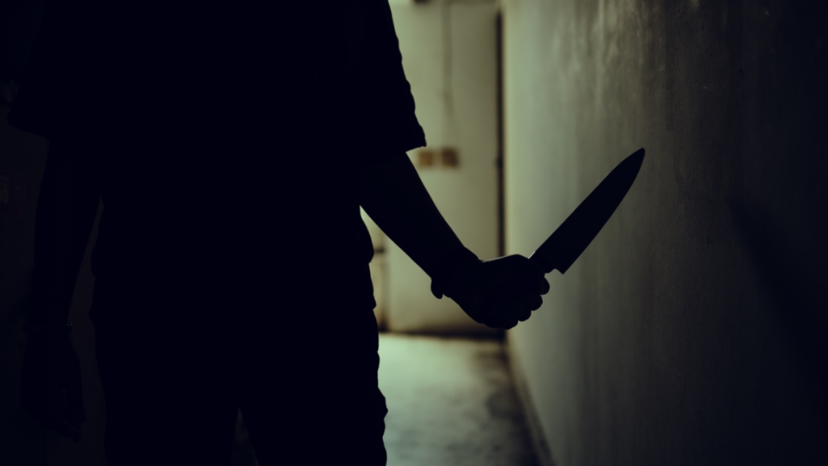 Die Silhouette einer Person mit Messer. In einem dunklen Gang.